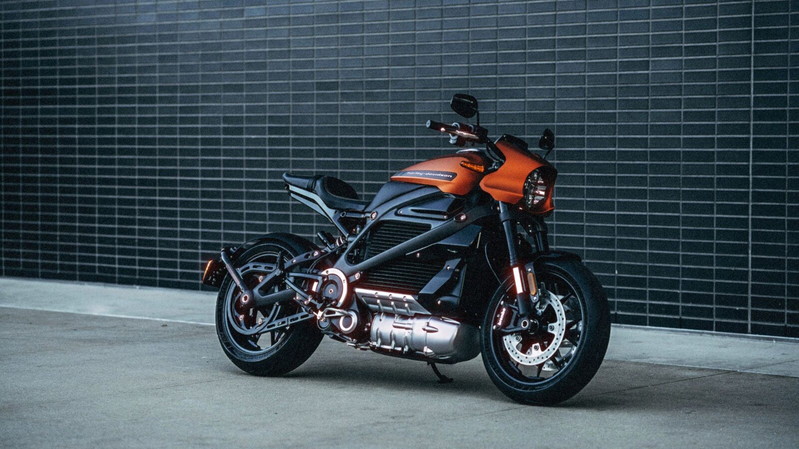 Orange electric motorcycle parked against a dark brick wall, processed with FilmGrainLab at ISO 400
